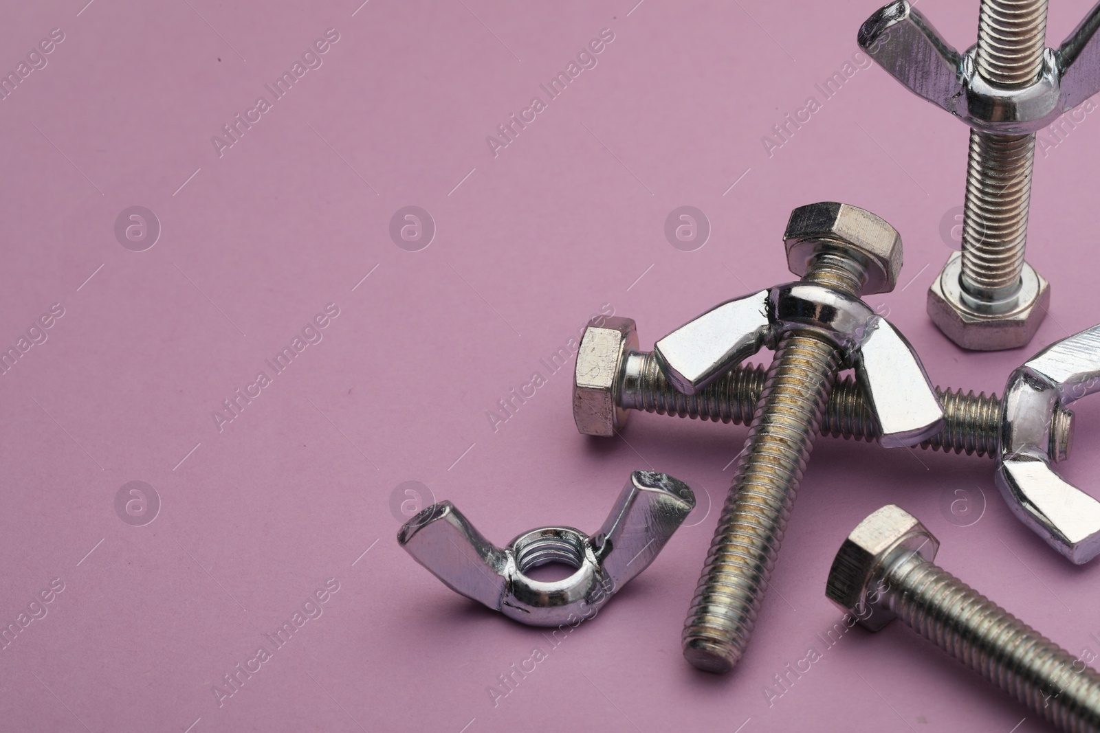 Photo of Metal screws with wing nuts on purple background, closeup. Space for text