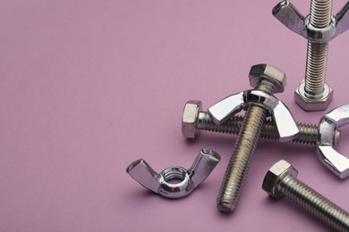 Metal screws with wing nuts on purple background, closeup. Space for text