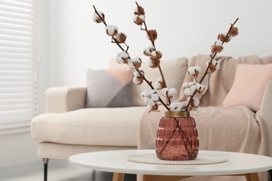 Cotton branches with fluffy flowers on white table in cozy room. Space for text