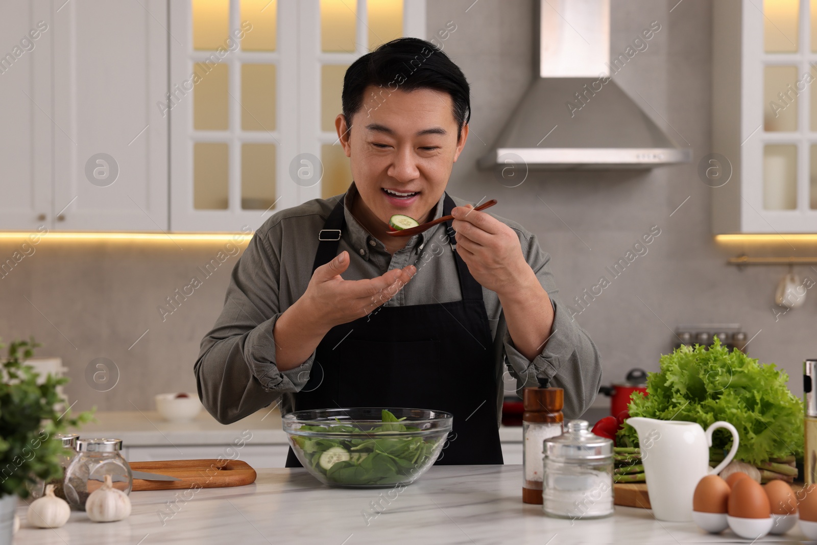 Photo of Cooking process. Man tasting salad in kitchen