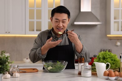 Cooking process. Man tasting salad in kitchen