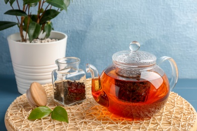 Photo of Teapot with hot aromatic tea, dry and fresh leaves on wicker mat