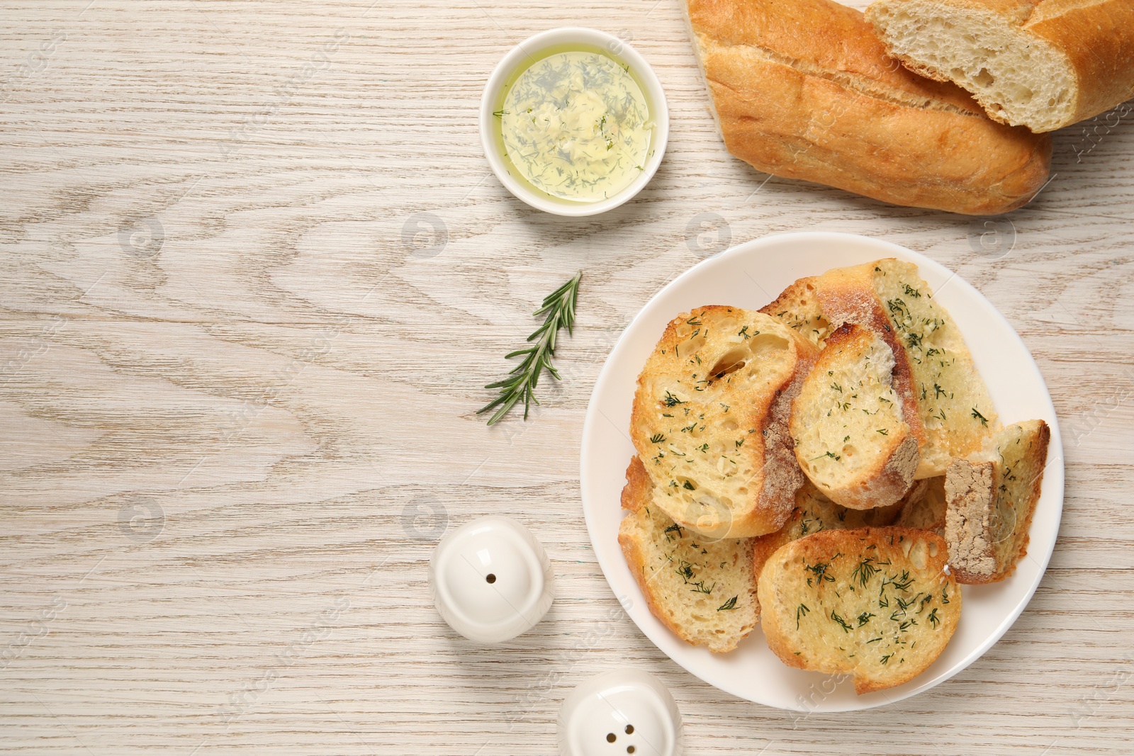 Photo of Tasty baguette with garlic, dill, rosemary and oil on white wooden table, flat lay. Space for text