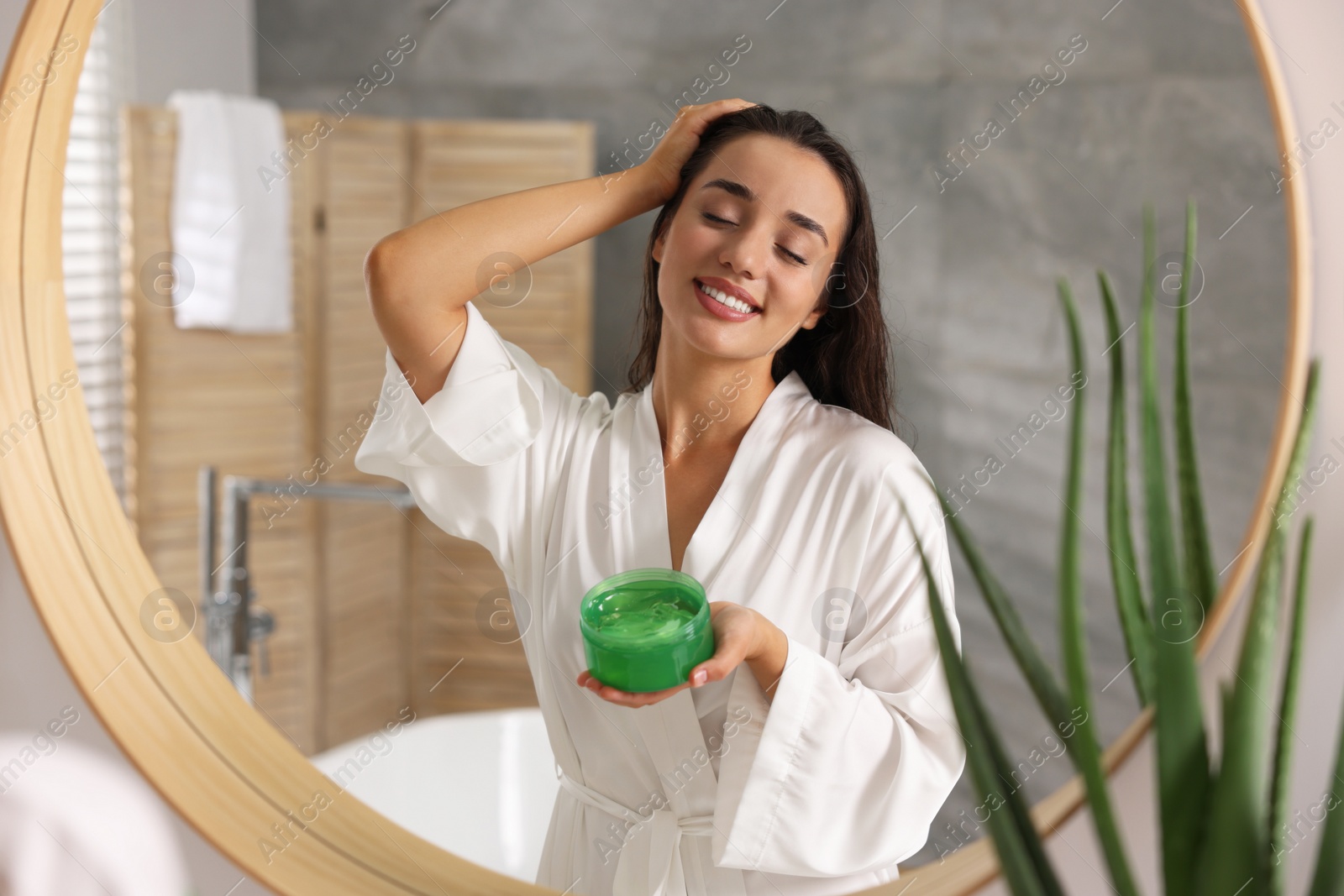 Photo of Young woman applying aloe hair mask near mirror in bathroom