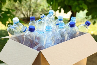 Photo of Cardboard box with used plastic bottles outdoors. Recycle concept