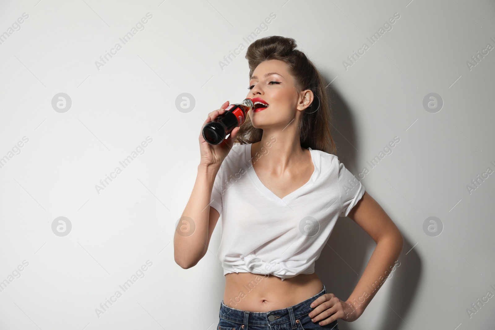 Photo of MYKOLAIV, UKRAINE - NOVEMBER 28, 2018: Young woman drinking Coca-Cola on white background