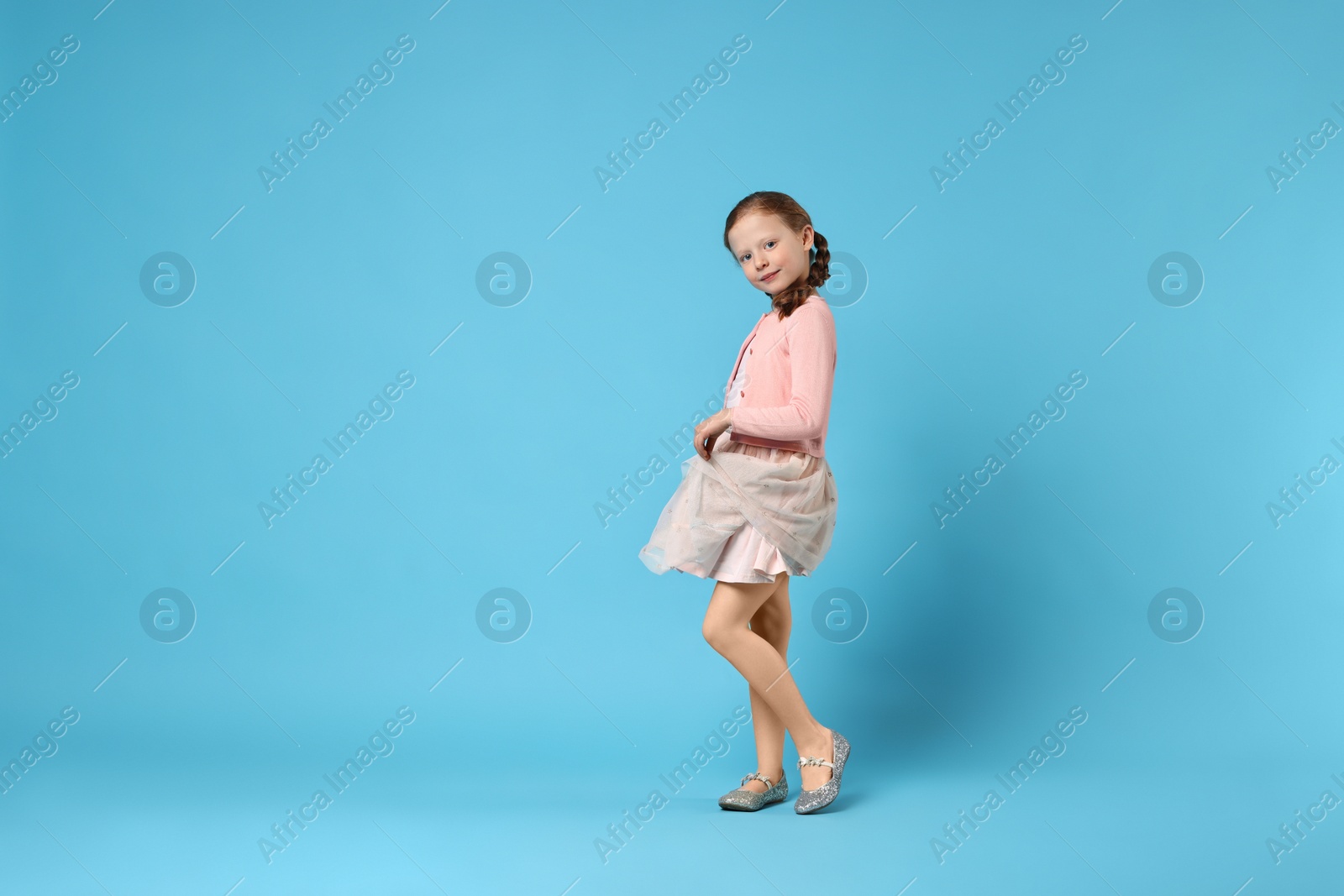 Photo of Cute little girl dancing on light blue background, space for text