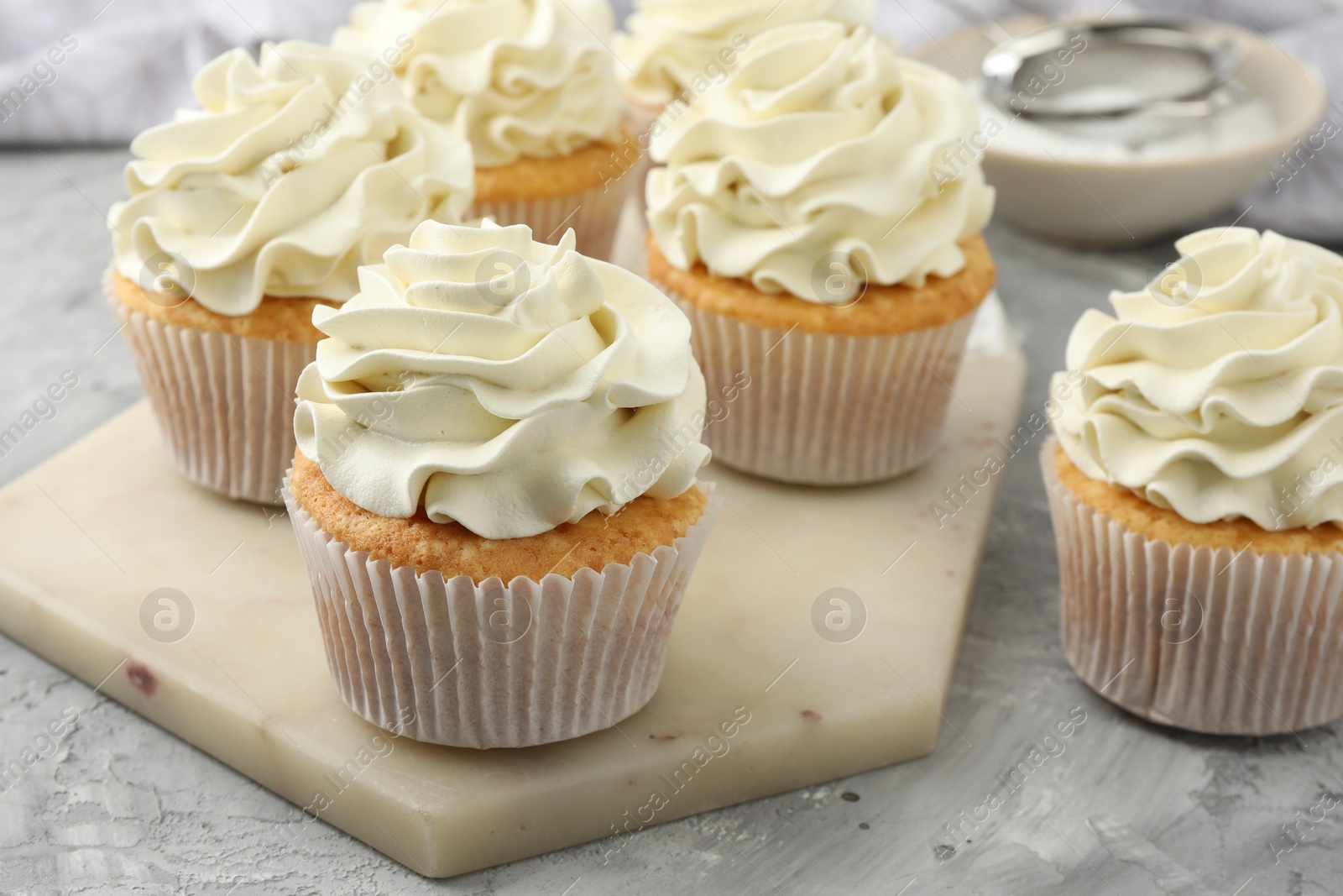 Photo of Tasty cupcakes with vanilla cream on grey table, closeup