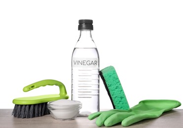 Photo of Natural cleaning products. Vinegar in bottle, baking soda, glove, sponge and brush on light wooden table against white background