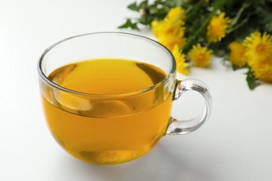 Photo of Delicious fresh tea and beautiful dandelion flowers on white background, closeup