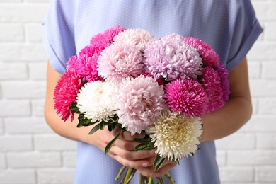 Woman holding beautiful aster flower bouquet against brick wall