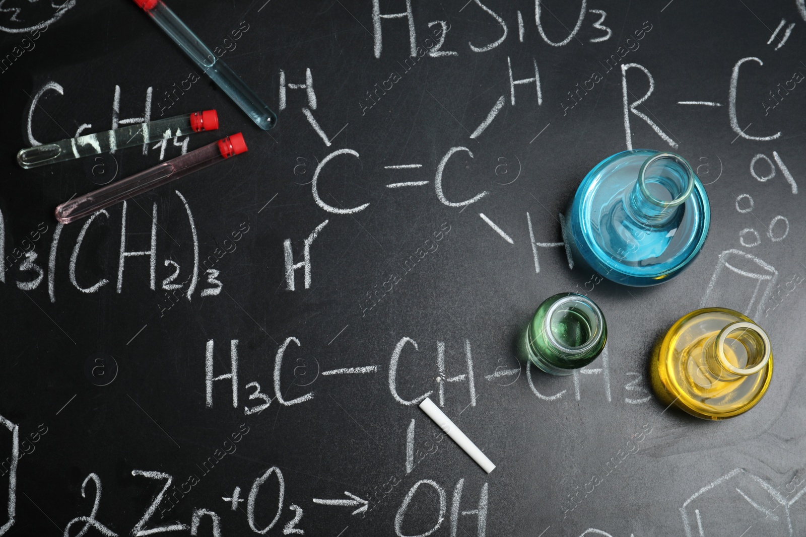 Photo of Laboratory glassware on blackboard with chemical formulas, flat lay