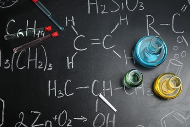 Laboratory glassware on blackboard with chemical formulas, flat lay