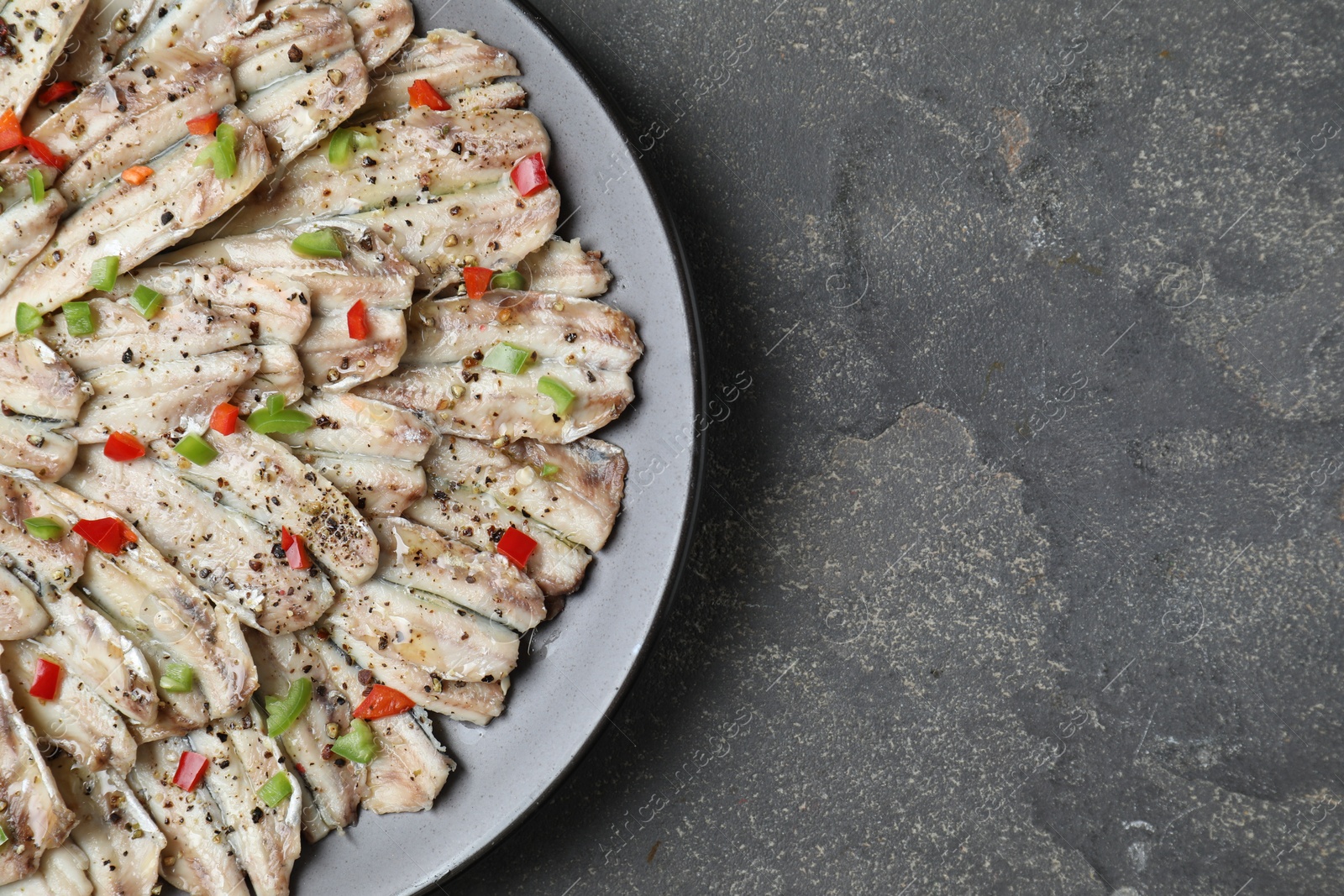 Photo of Tasty pickled anchovies with spices on grey textured table, top view. Space for text