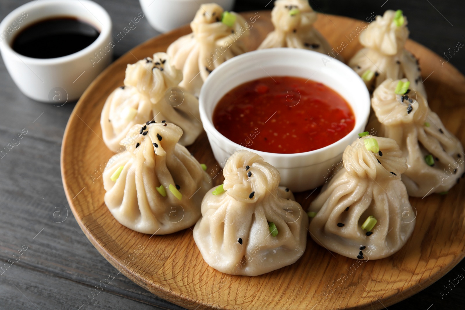 Photo of Wooden plate with tasty baozi dumplings and sauce on table, closeup