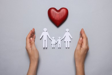 Photo of Woman protecting paper family cutout on grey background, top view. Insurance concept