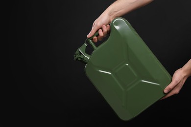 Man holding khaki metal canister on black background, closeup. Space for text