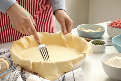 Woman making holes in raw dough with fork at white table, closeup. Baking meat pie