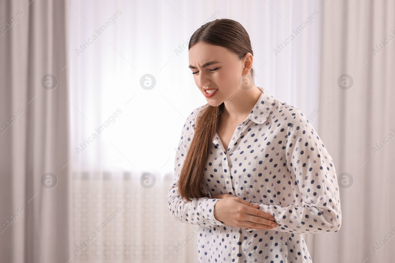 Photo of Young woman suffering from stomach pain at home. Space for text