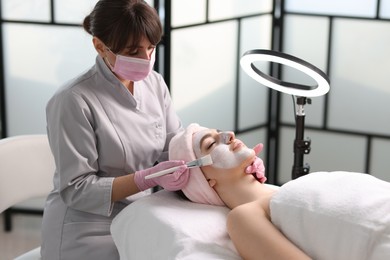 Photo of Cosmetologist applying mask on woman's face in clinic