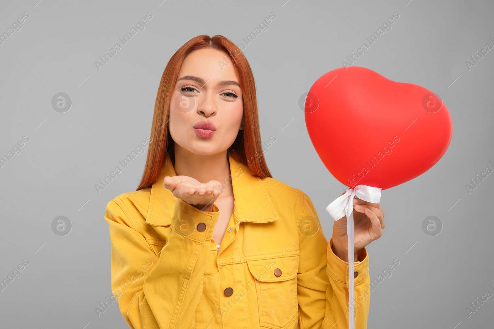 Photo of Beautiful woman with red heart shaped balloon blowing kiss on grey background