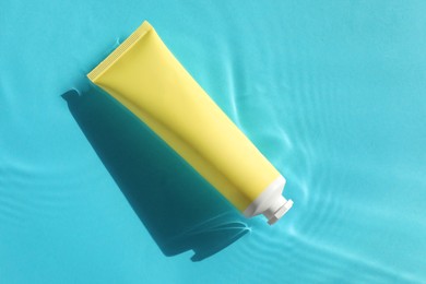 Tube with moisturizing cream in water on light blue background, top view