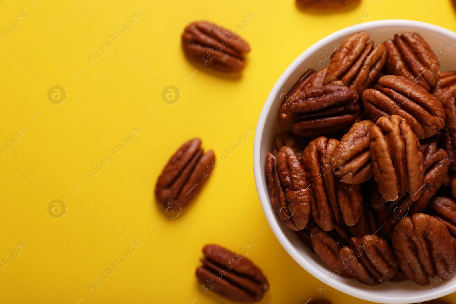 Photo of Bowl with tasty nuts on yellow background, flat lay. Space for text