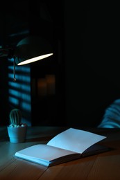Photo of Open book and cactus on wooden table at night