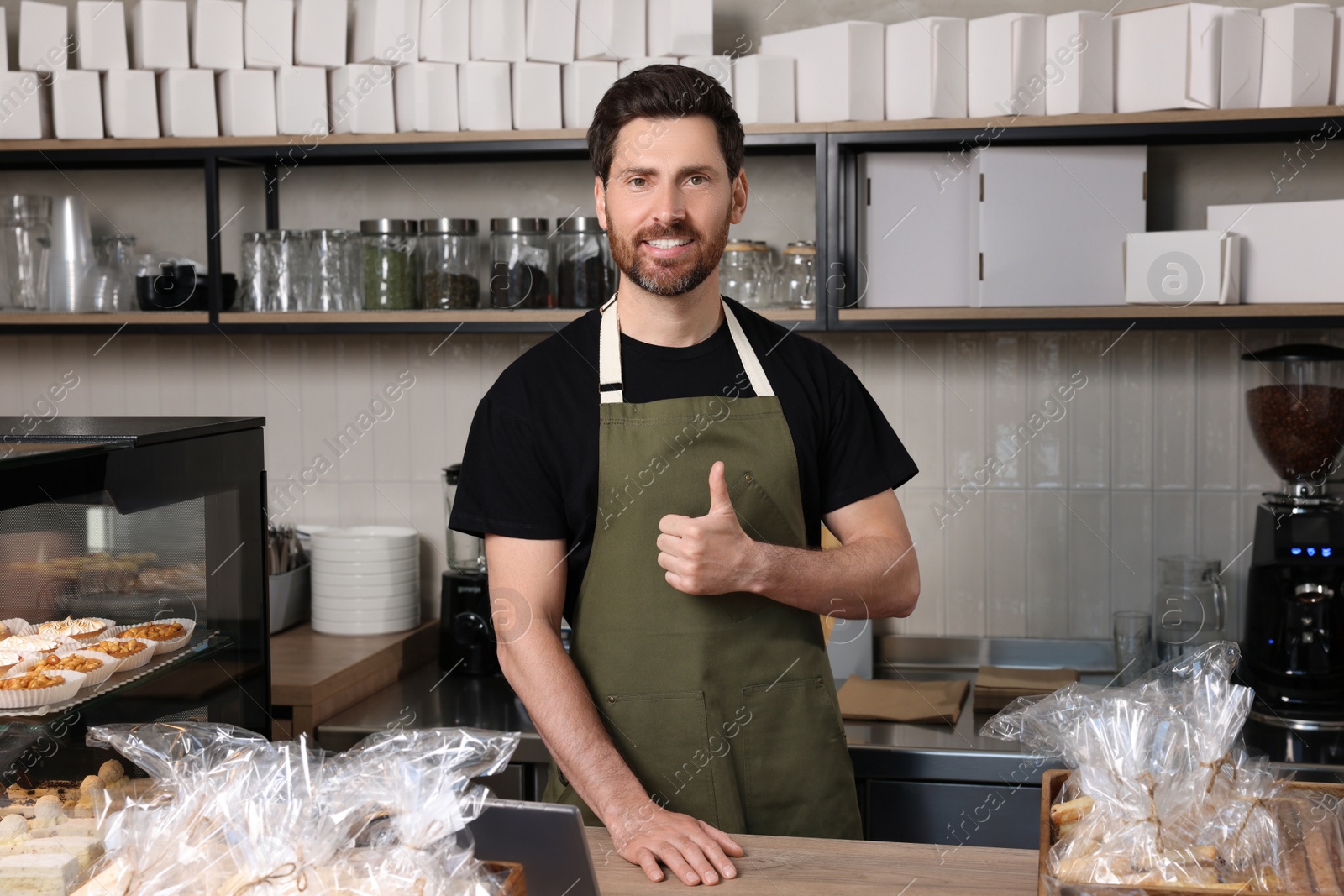 Photo of Happy seller showing thumb up at cashier desk in bakery shop