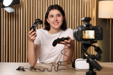 Photo of Smiling technology blogger with game controllers recording video review at home