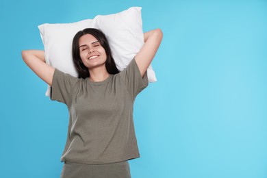 Sleepy young woman with soft pillow on light blue background, space for text