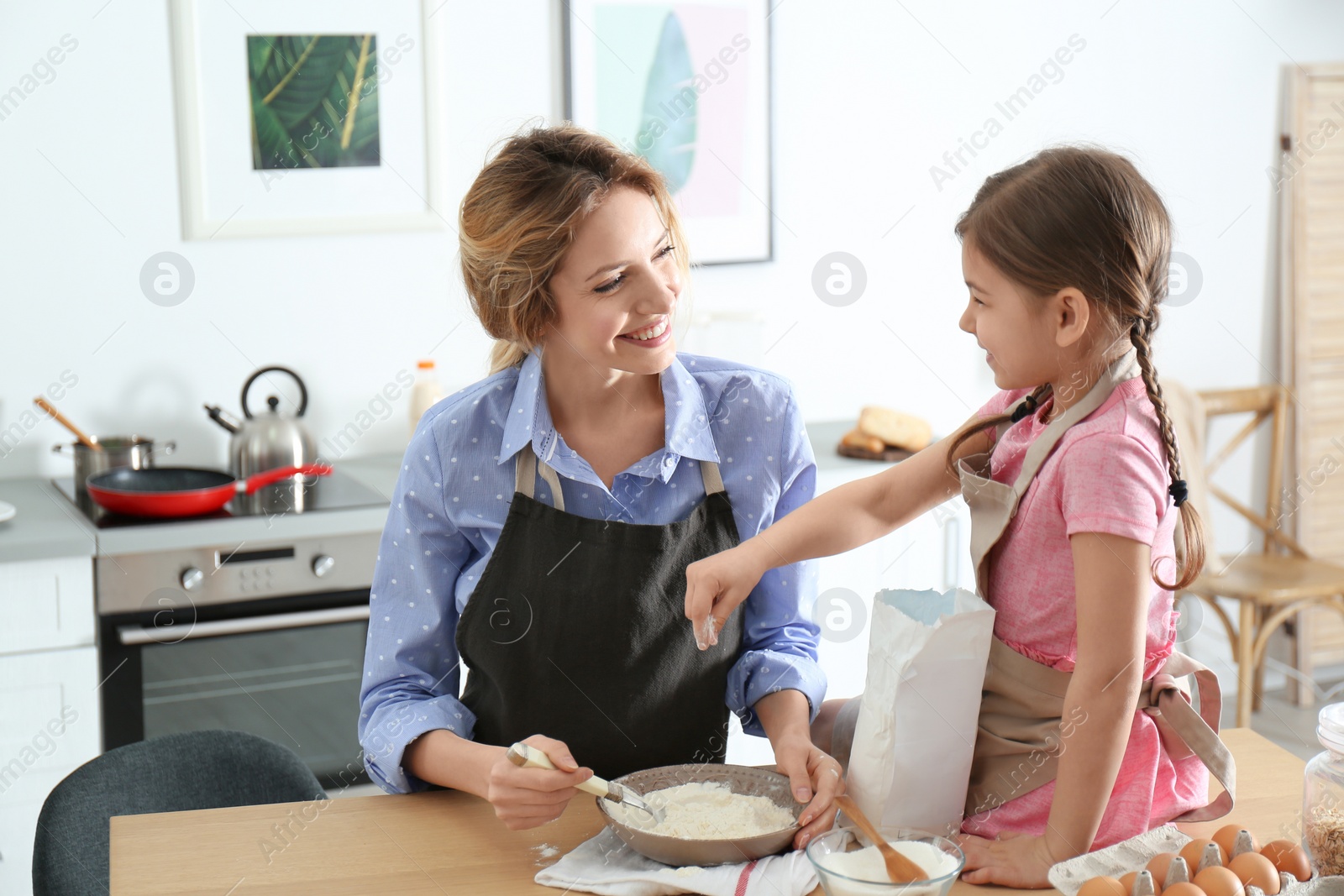 Photo of Young nanny with cute little girl cooking together in kitchen