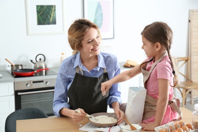 Young nanny with cute little girl cooking together in kitchen