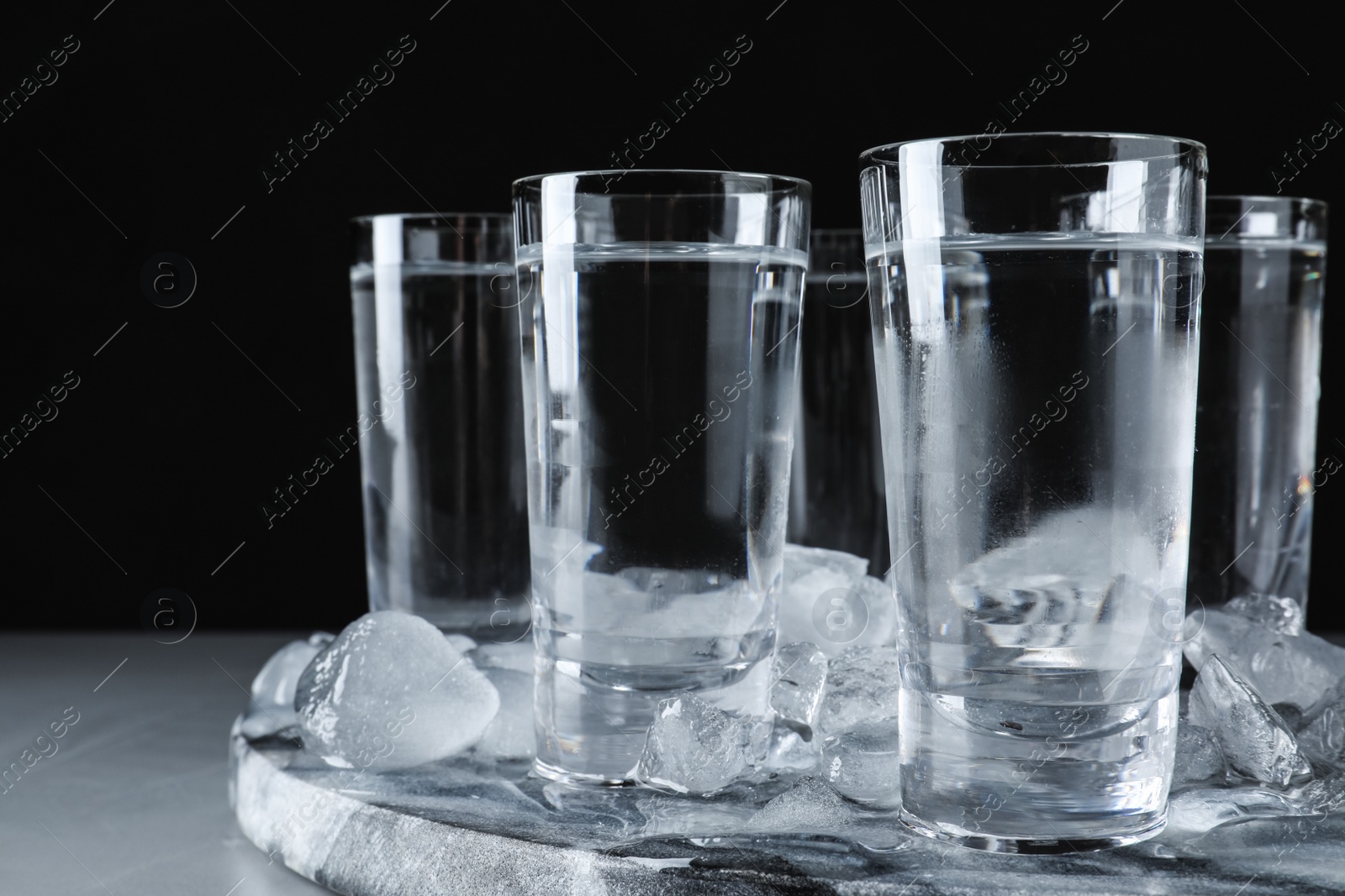 Photo of Vodka in shot glasses and ice on grey table, closeup