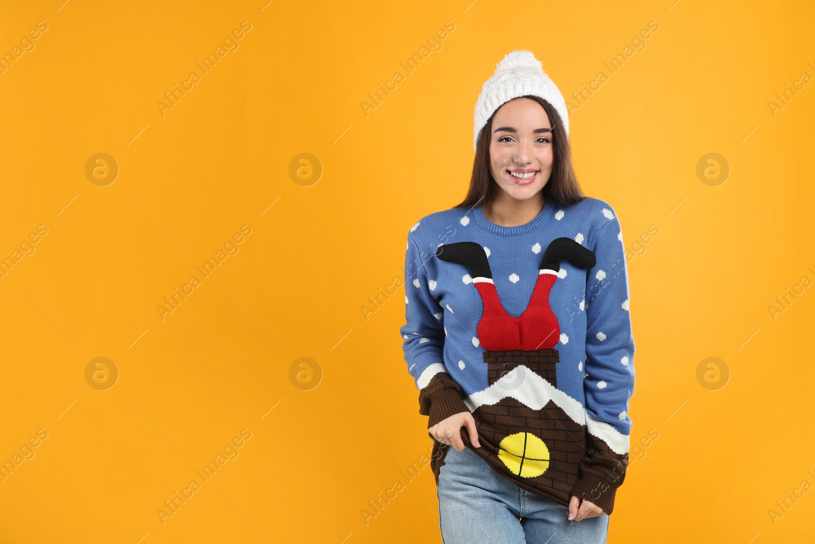 Photo of Young woman in Christmas sweater and hat on yellow background, space for text