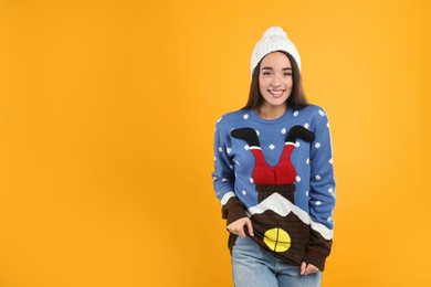 Young woman in Christmas sweater and hat on yellow background, space for text
