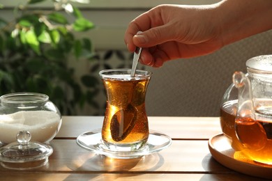 Woman stirring sugar in tea at wooden table indoors, closeup