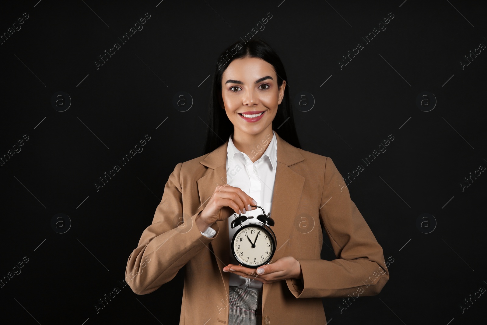 Photo of Businesswoman holding alarm clock on black background. Time management