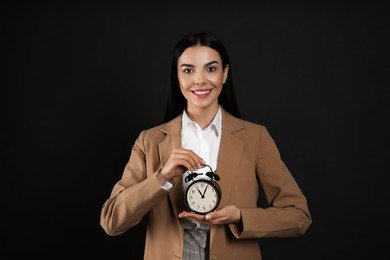 Photo of Businesswoman holding alarm clock on black background. Time management