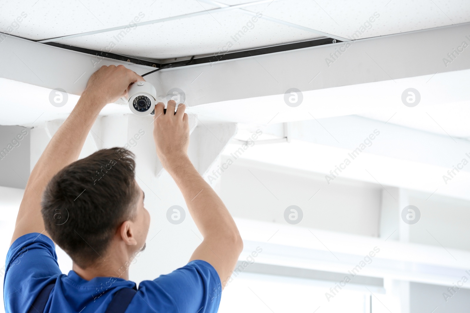 Photo of Technician installing CCTV camera on ceiling indoors