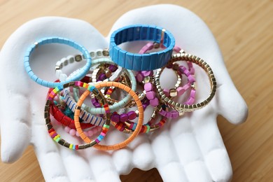 Photo of Ceramic hand stand with many stylish bracelets on wooden table, closeup