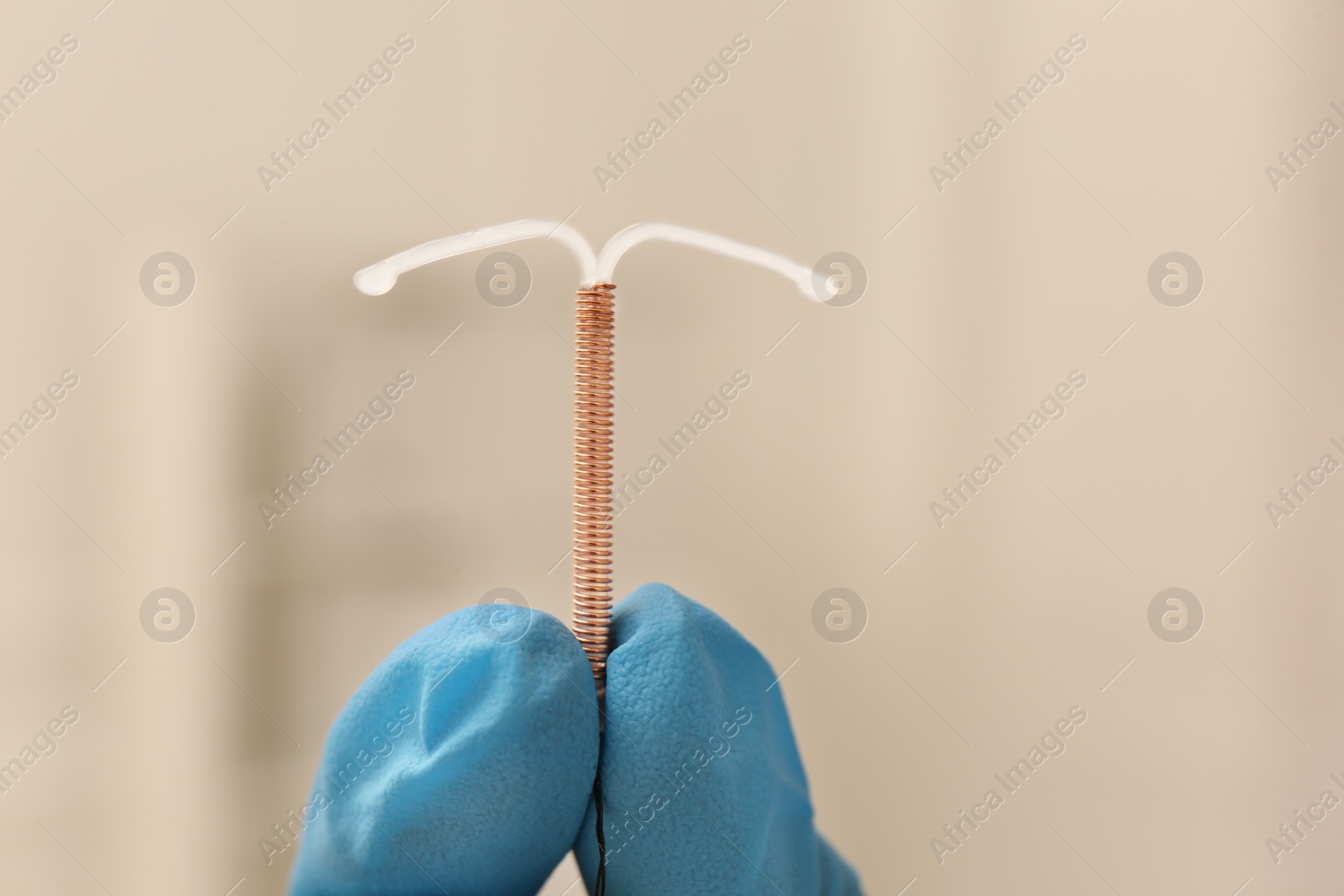 Photo of Doctor holding T-shaped intrauterine birth control device on blurred background, closeup