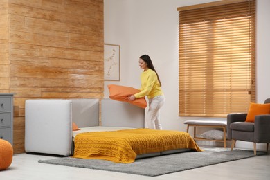 Photo of Young woman making bed in room. Modern interior with sleeper sofa
