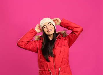 Happy young woman in warm clothes on pink background. Winter vacation