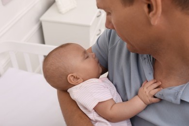 Happy father with his cute sleeping baby near crib at home