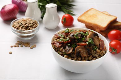 Delicious lentils with mushrooms, bacon and green onion in bowl served on white table, closeup