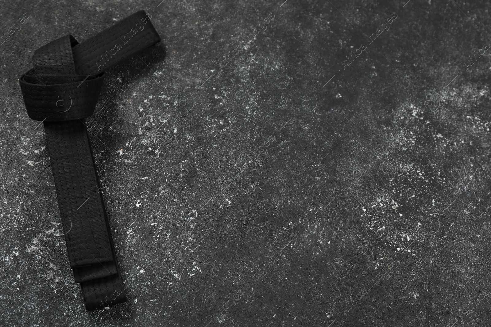 Photo of Black karate belt on gray textured background, top view. Space for text