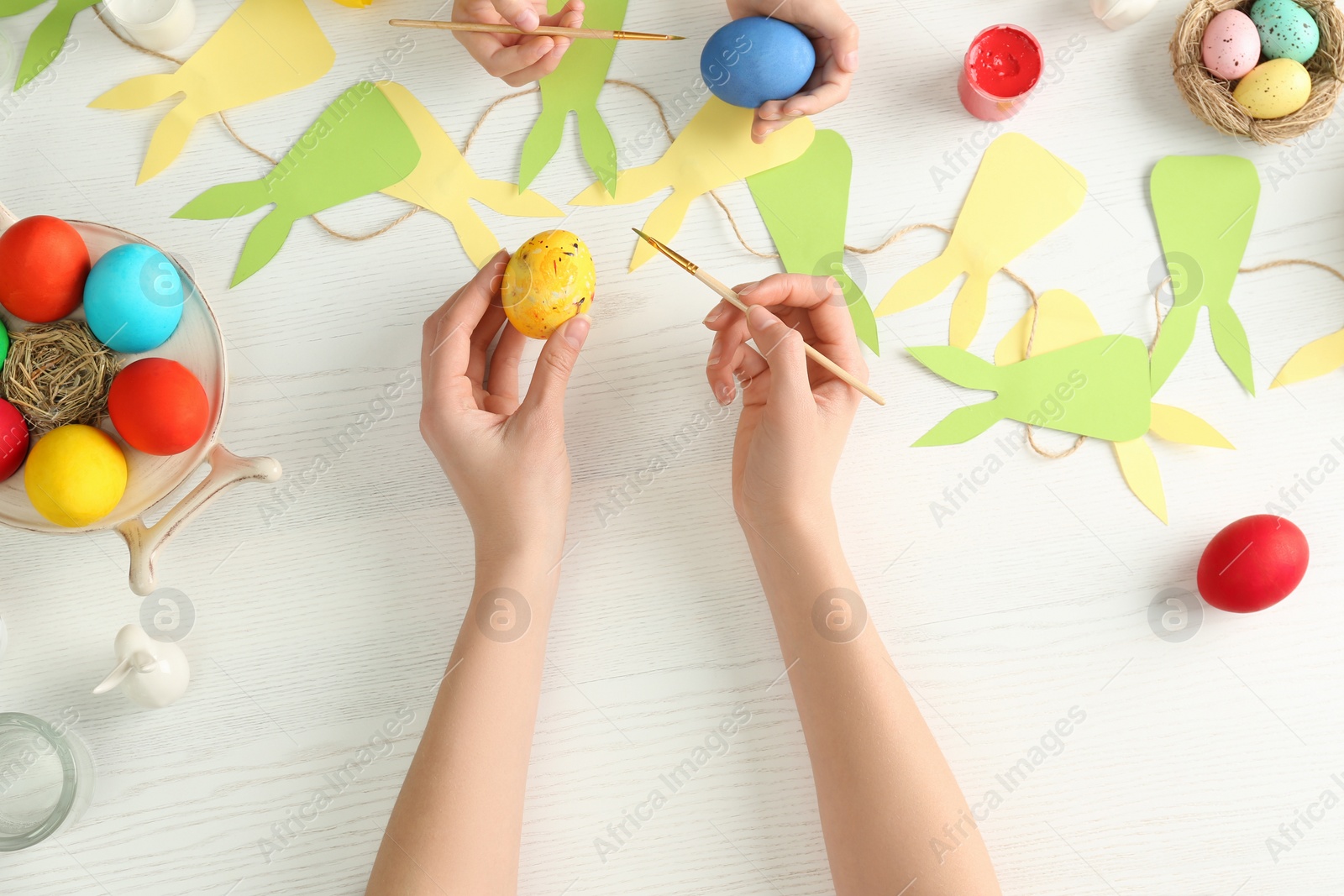 Photo of Mother and her child painting Easter eggs at table, top view