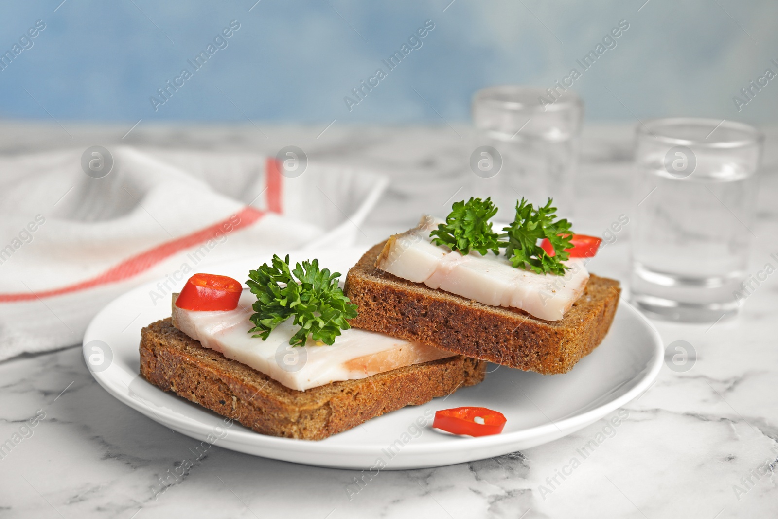 Photo of Plate with pork fatback sandwiches and shots of vodka on marble table