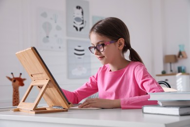 Little girl doing homework with tablet at table in room